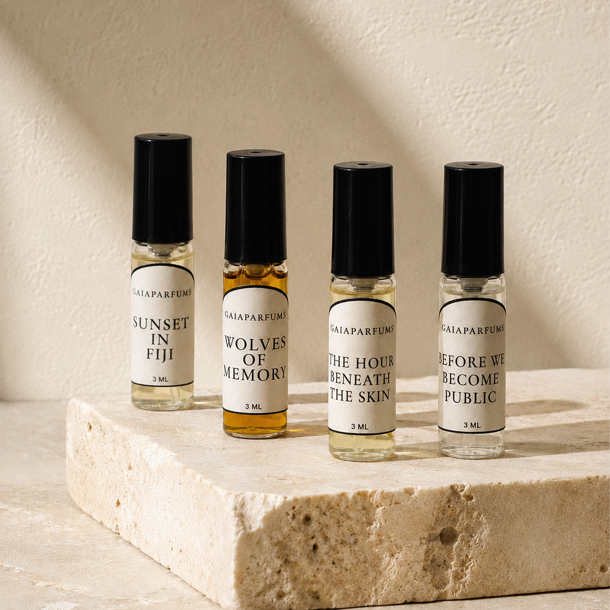Four 3ml GAIA Parfums sample bottles with black caps and white labels, arranged on a light stone slab against a textured beige wall. The labels read Sunset in Fiji, Wolves of Memory, The Hour Beneath the Skin, and Before We Become Public.