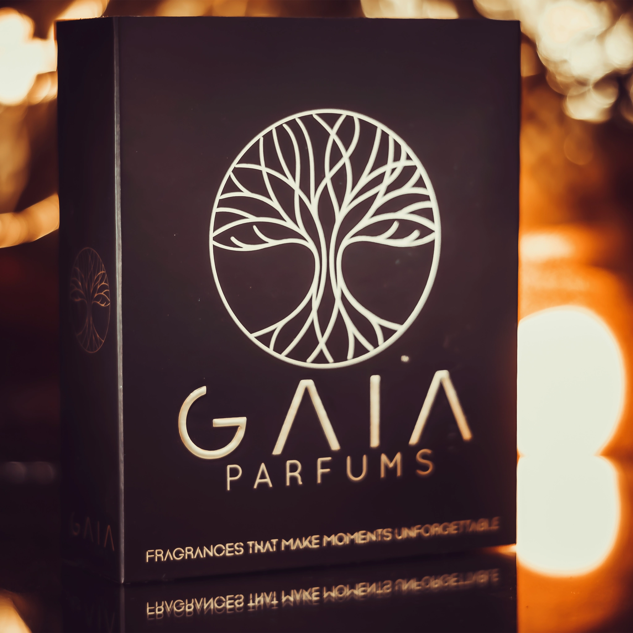 A dark brown rectangular box for GAIA PARFUMS with a tree of life logo and text, set against a warm, blurred bokeh background.