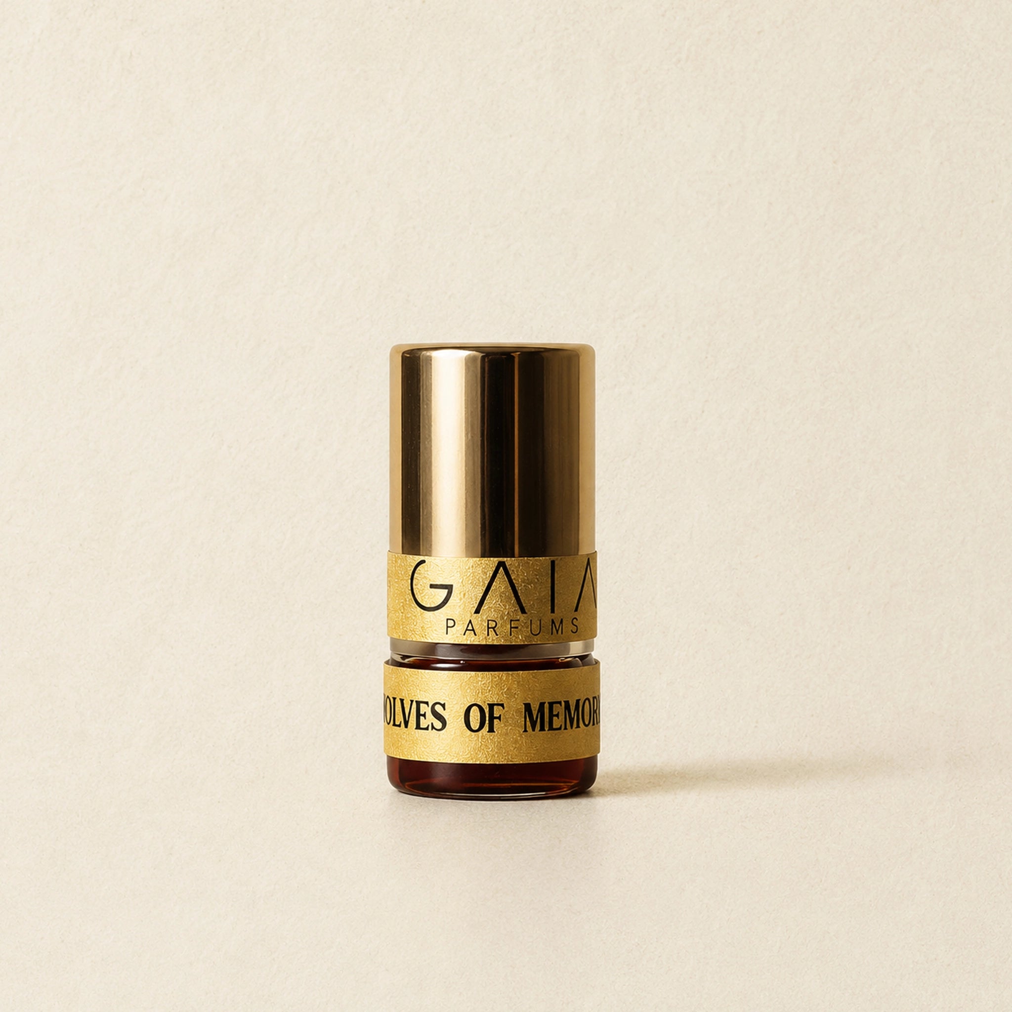 A 1 gm Attar bottle with a shiny gold cap and a gold label reading 'GAIA PARFUMS' and 'WOLVES OF MEMORY', centered on a warm beige textured background.
